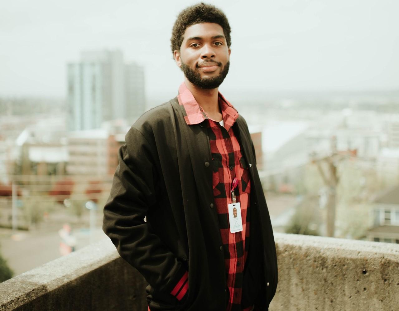 student wearing a red flannel and black jacket poses against a city skyline 