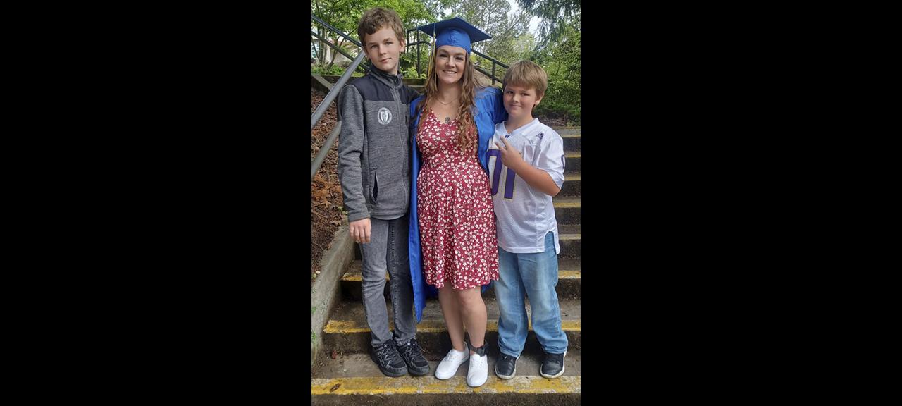  student in grad regalia poses with two young boys